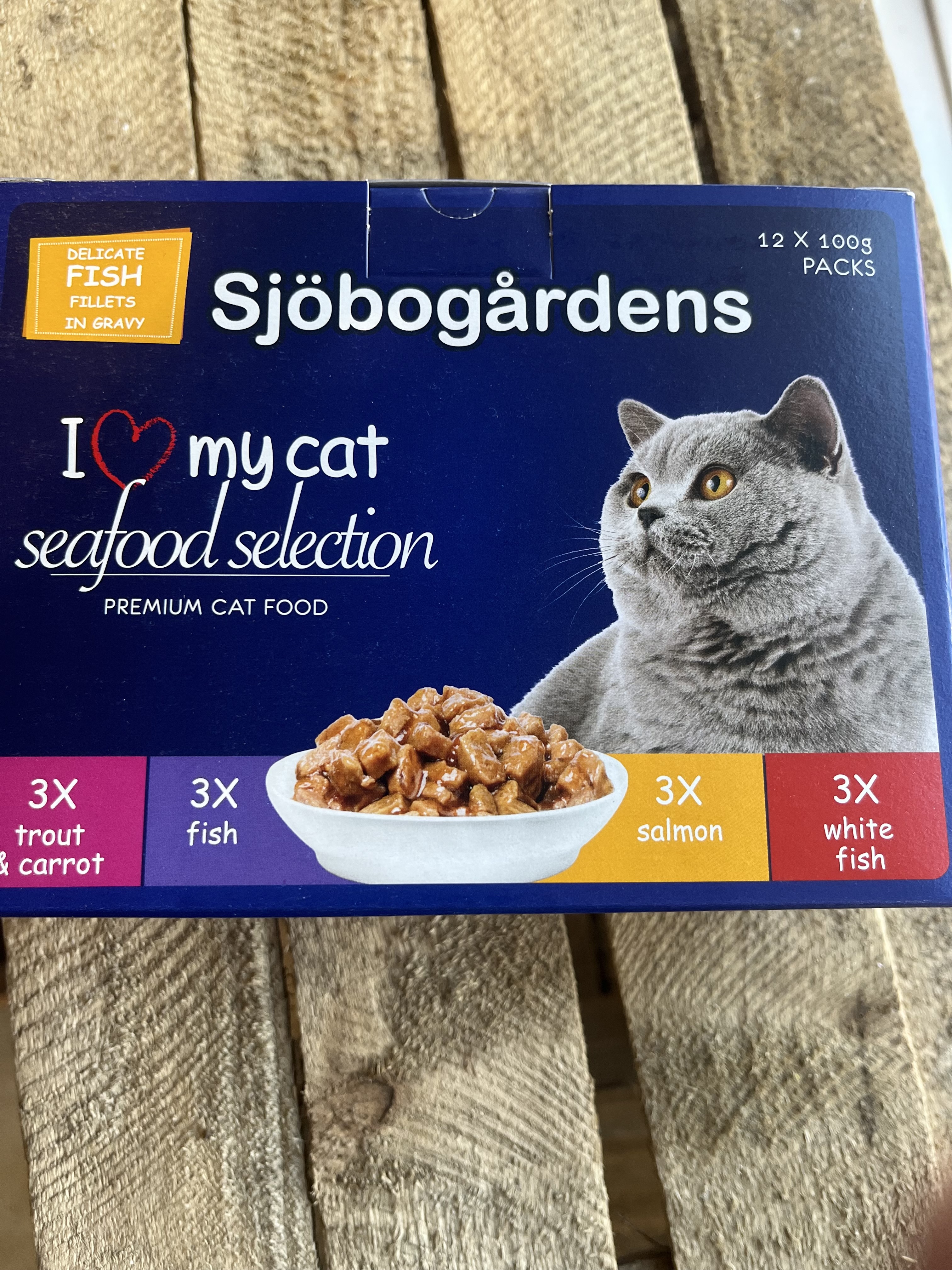 Blå ask med Kattmat 12p Fiskmeny Ocean Fantasy 1,2 kg med en grå katt och skaldjursbitar.