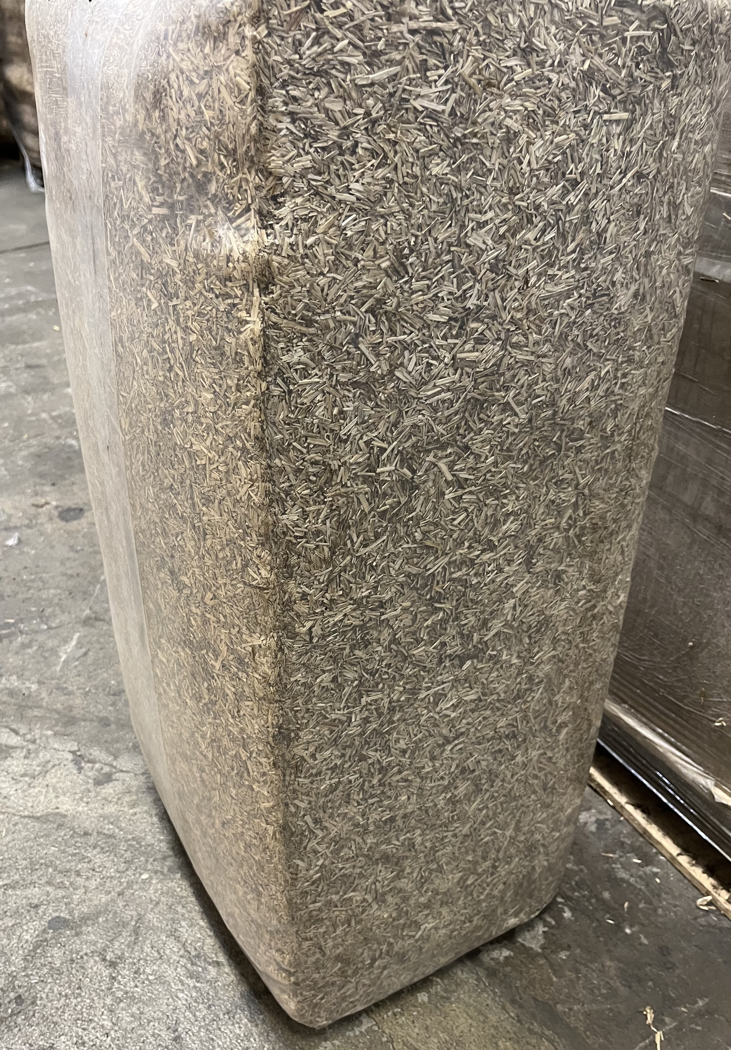 En stor, tätt packad Hampaströ 25 kg-bal står på ett betonggolv.