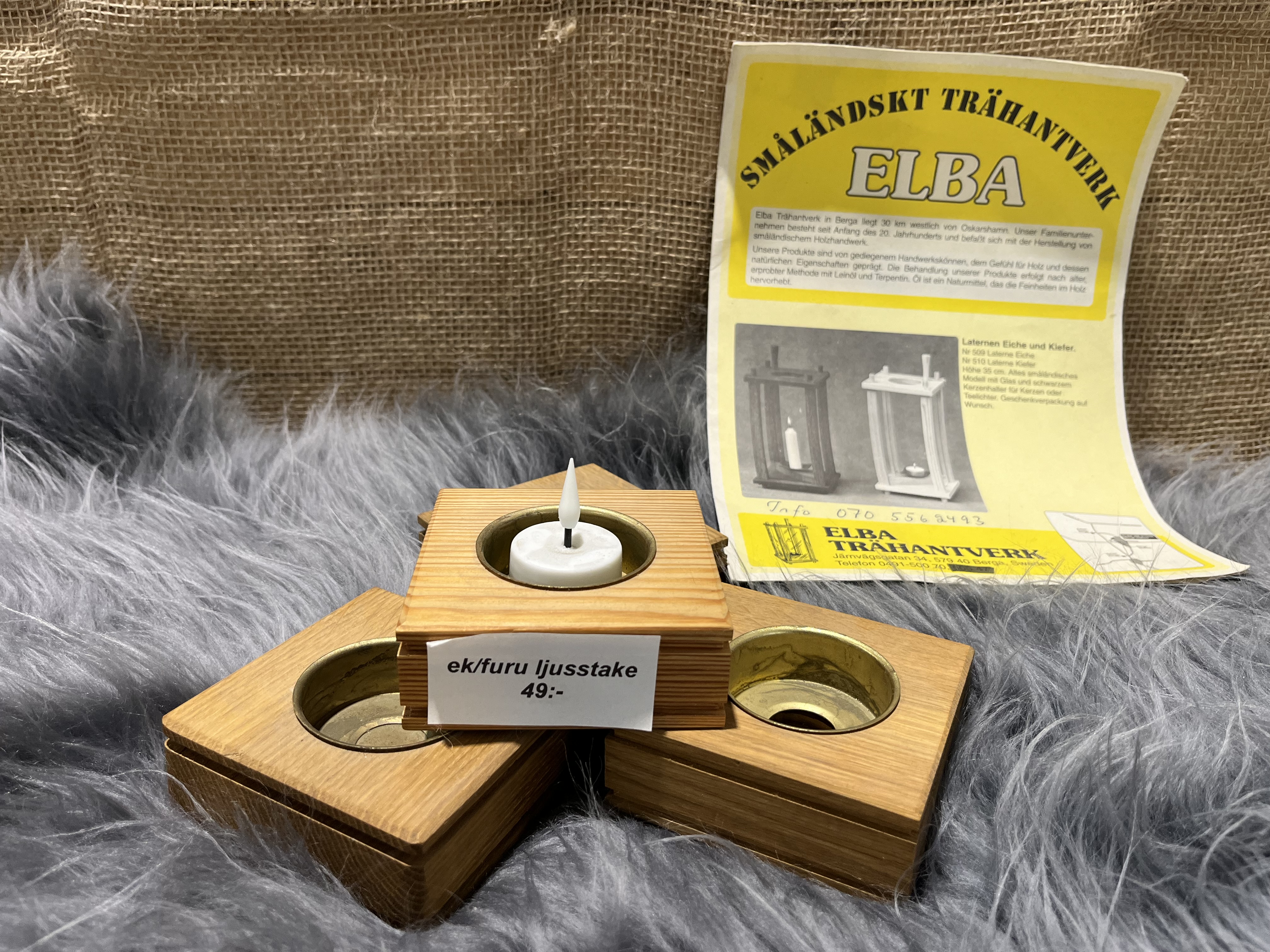 Tre ljusstakar Trä Ljusstake ek med värmeljus, prislapp och gul broschyr bakom.