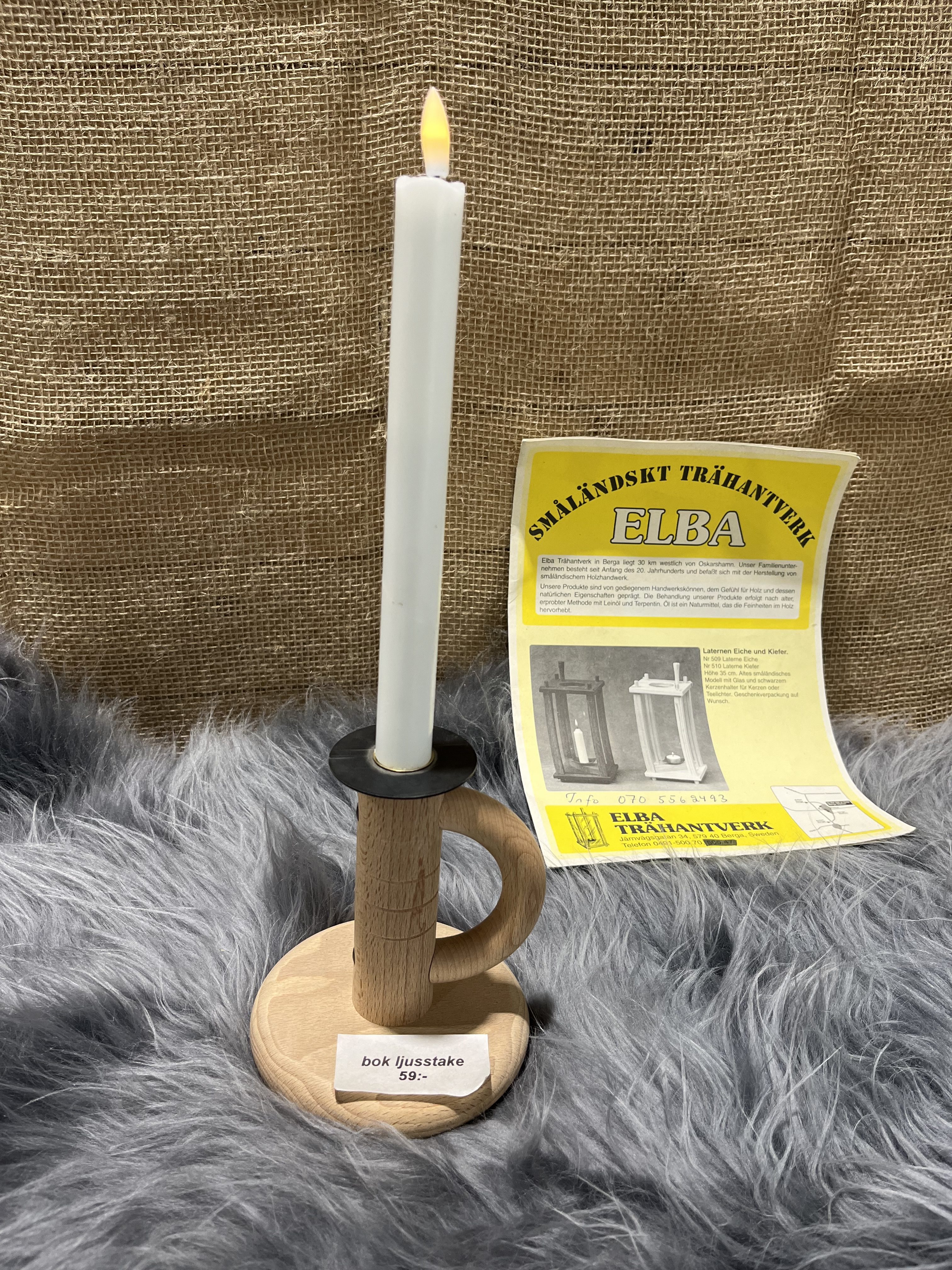 Trä ljustake bok med ett tänt vitt ljus på en luddig yta, broschyr i bakgrunden.