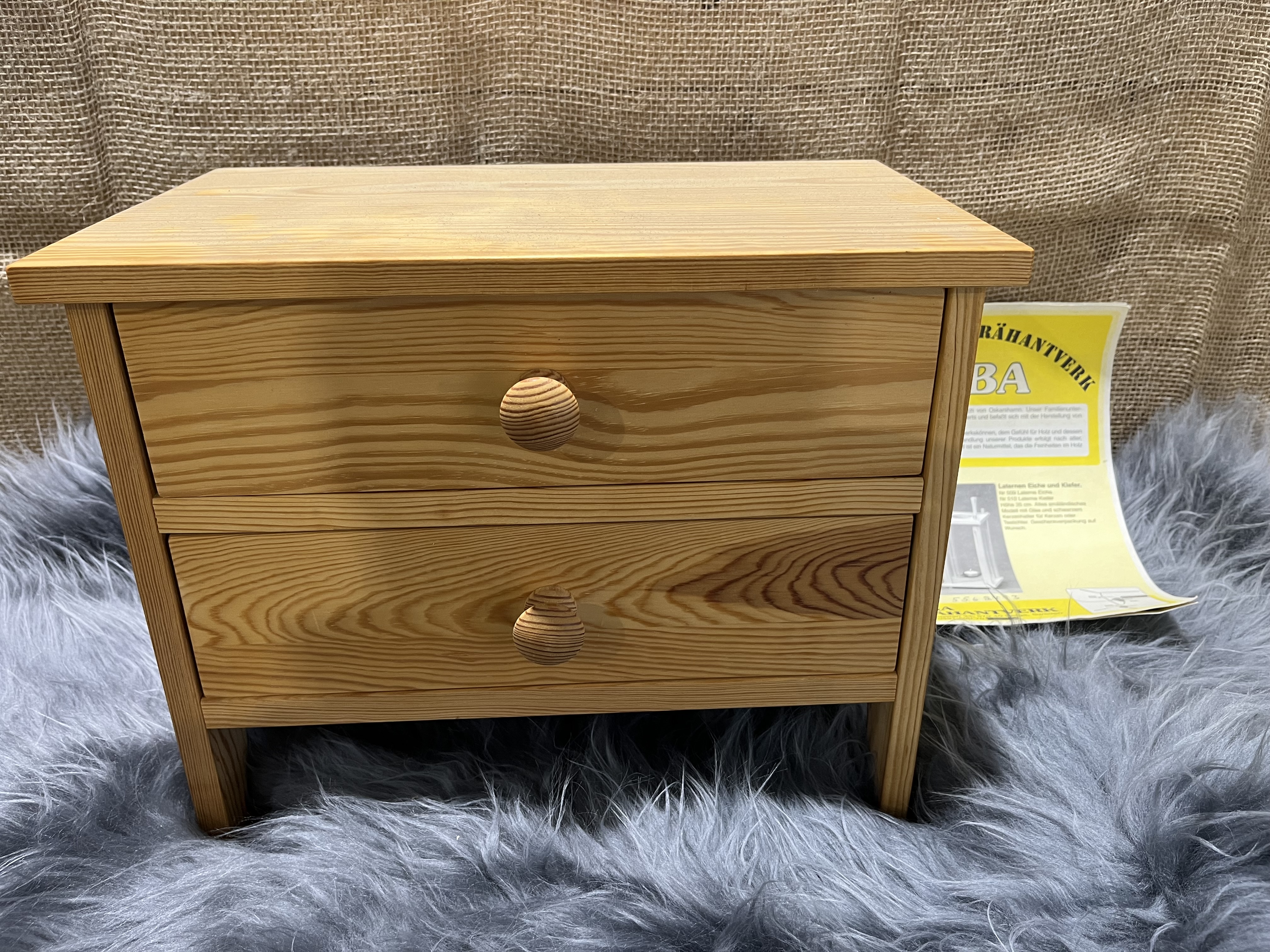 Träbyrå 2 lådor, en liten träkista, på grå pälsmatta med gul pappersbakgrund.