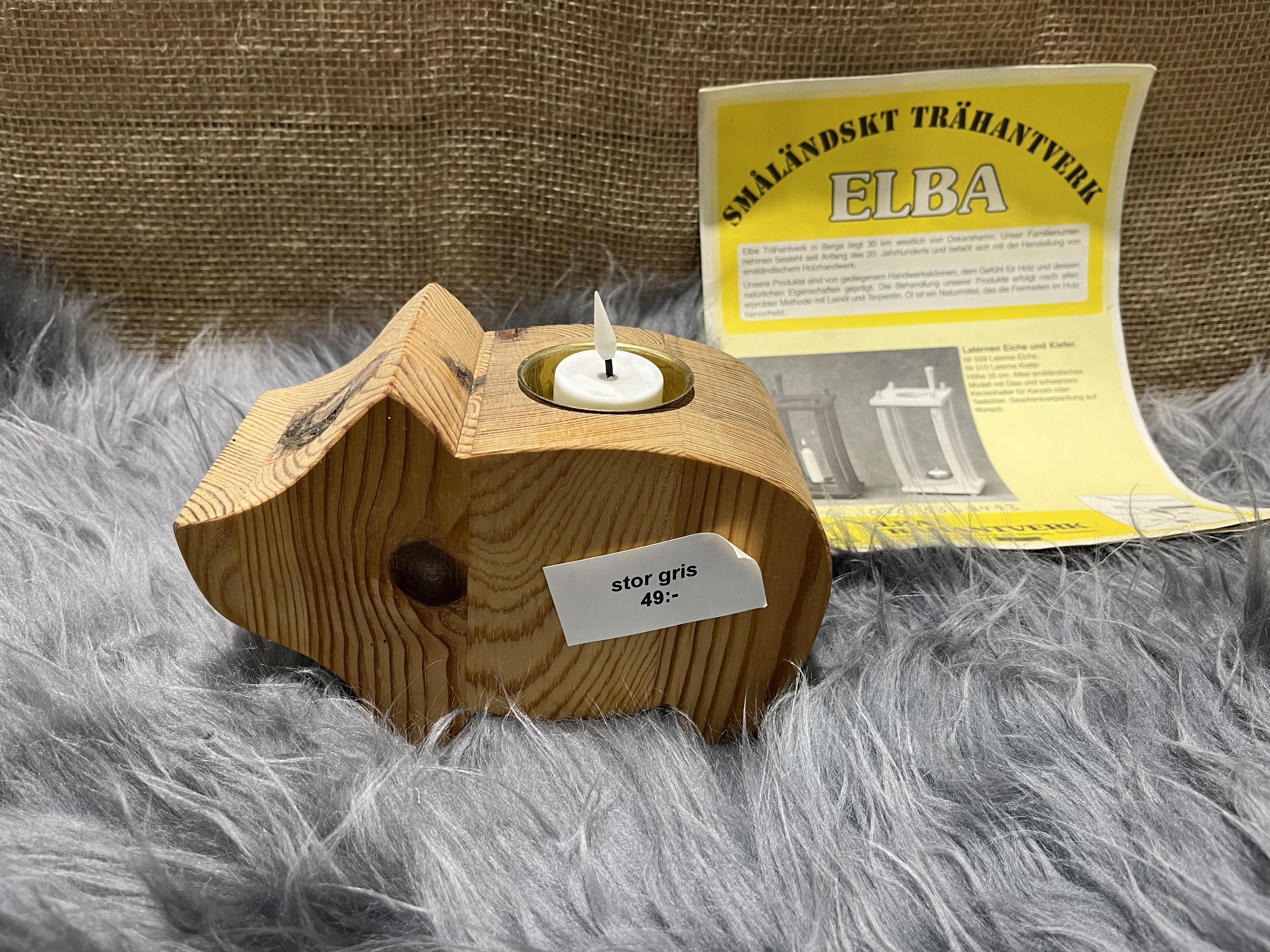 Trä gris stor trägris ljusstake med värmeljus och etikett, på päls med gul flyer.