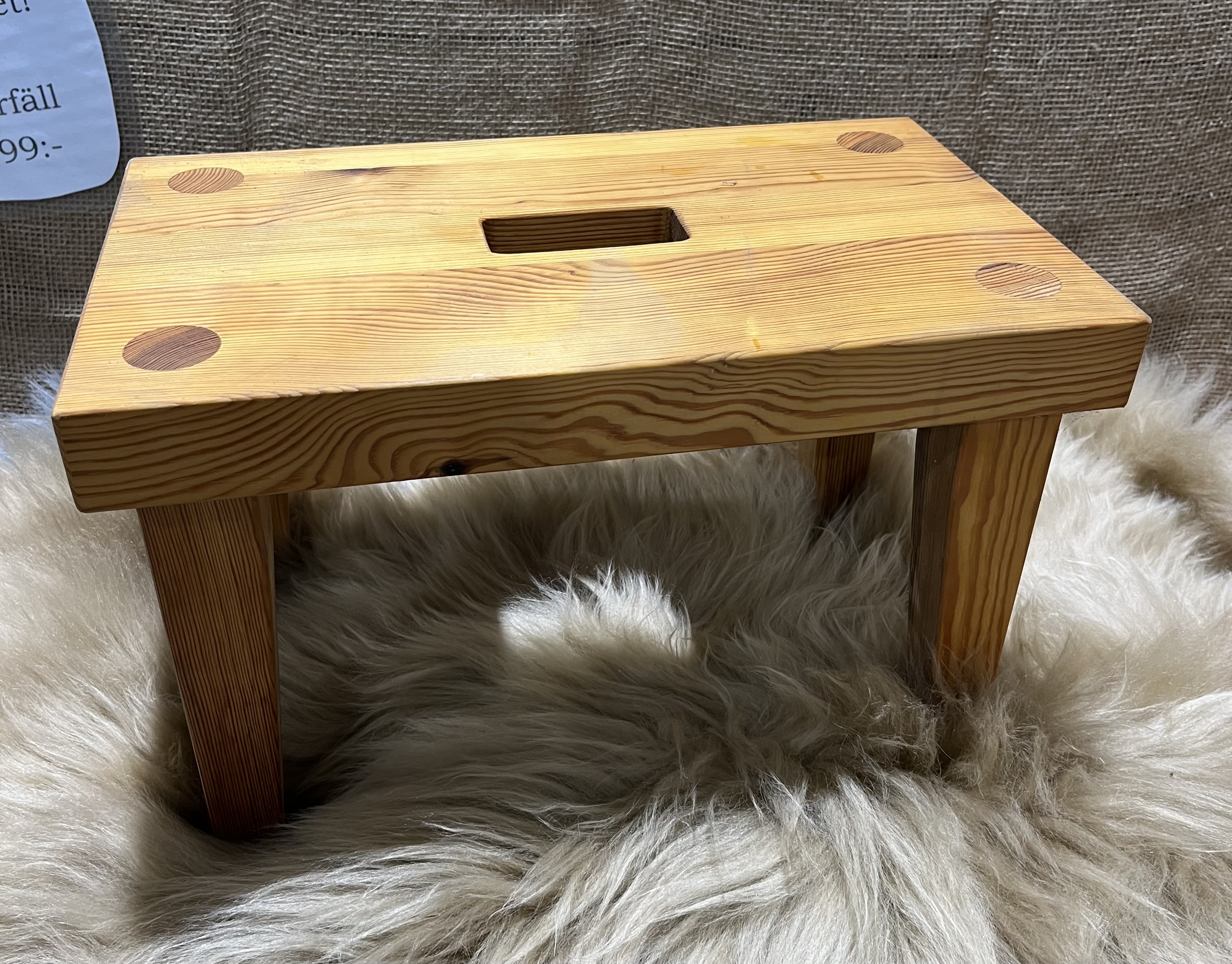 Trä Pall, en liten träpall med handtag, står på en fluffig matta.