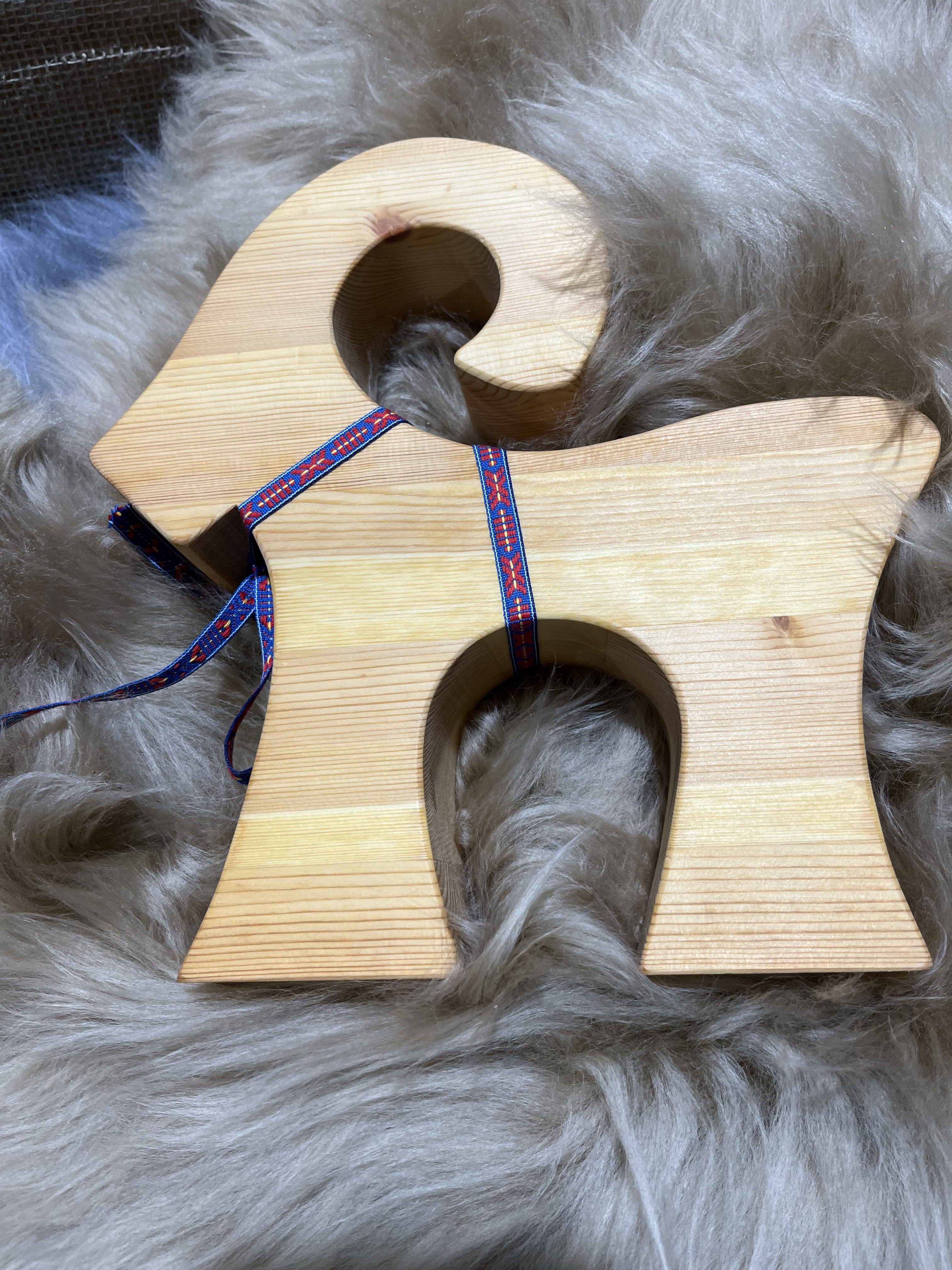 Trä bock stor med ett blått och rött band vilar på en fluffig grå yta.