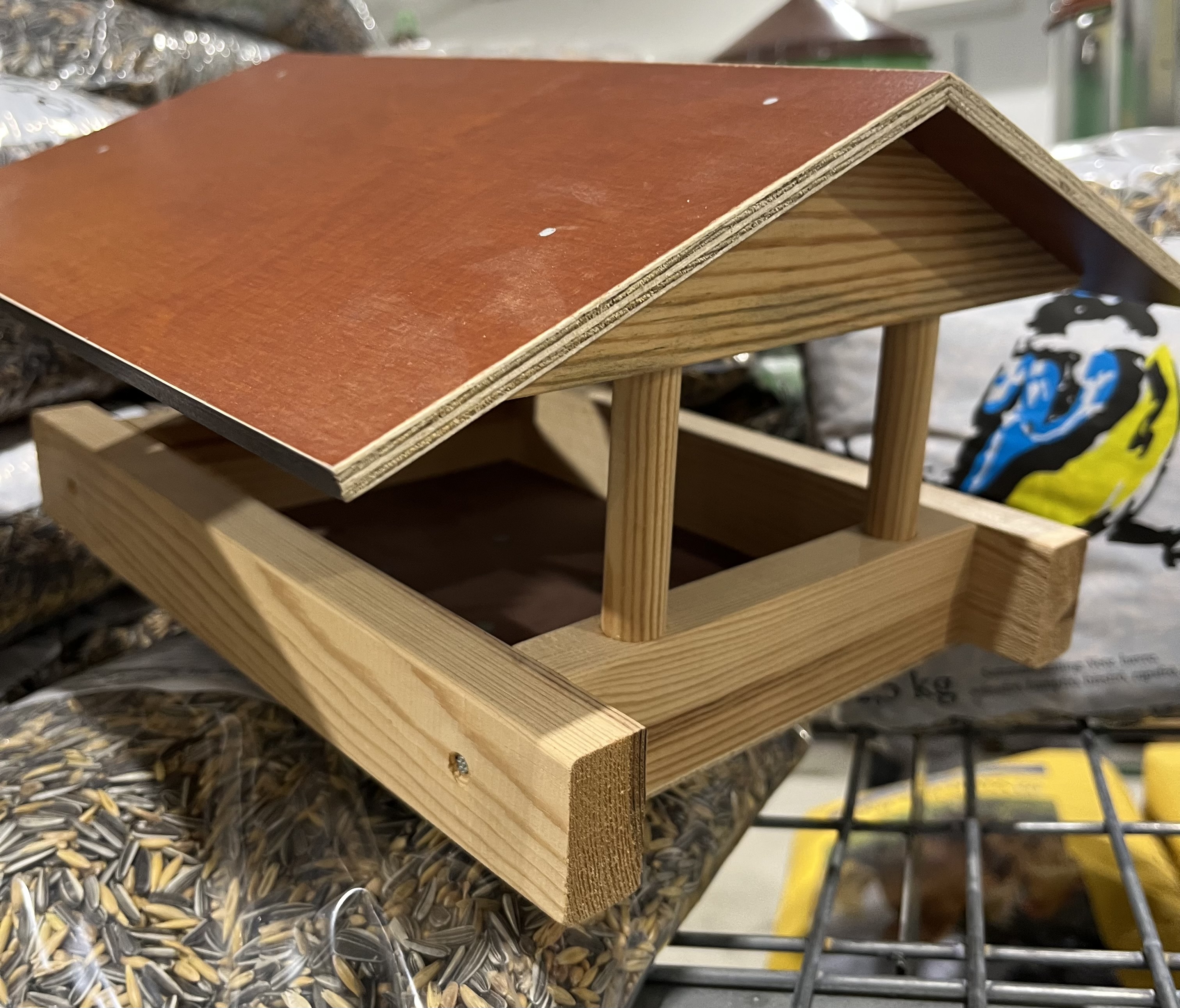 Trä Fågelbord med rött tak som visas på fågelfröpåsar i en butik.