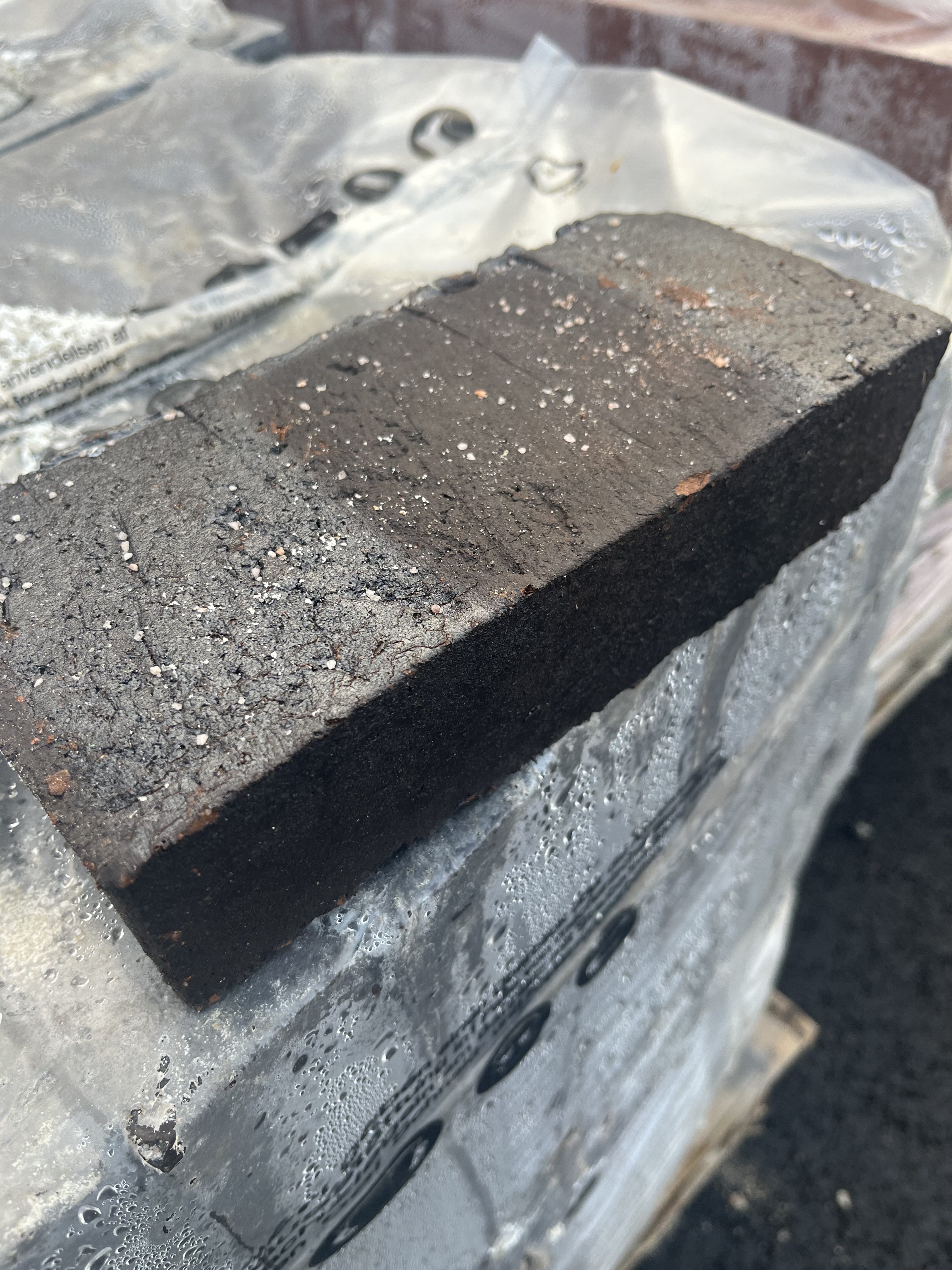 En enda Tegel SVART tegelsten sitter ovanpå en plastinpackad stapel med vattendroppar.