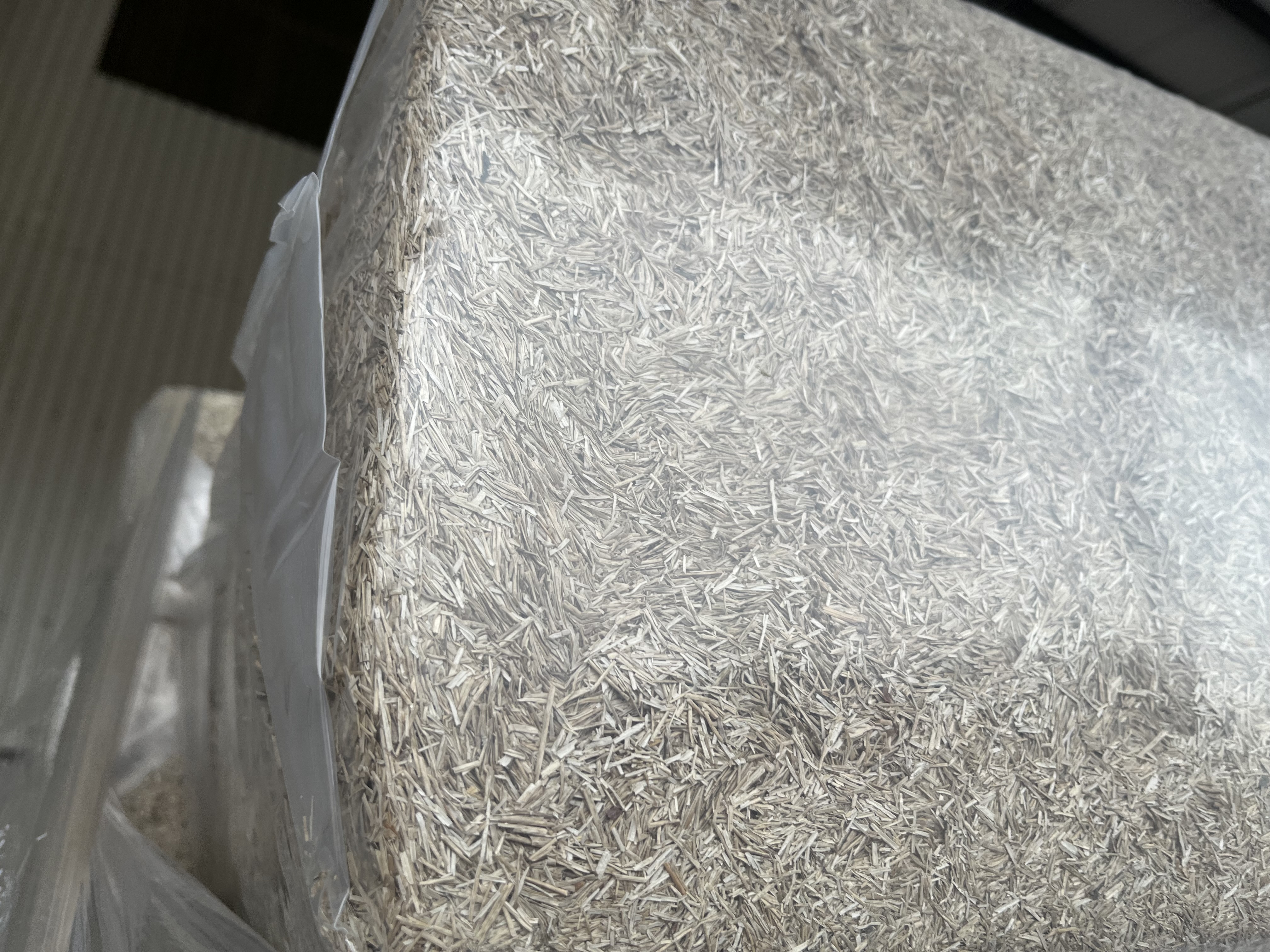 En närbild av en stor, genomskinlig plastinpackad bal av halm eller strimlat växtmaterial.