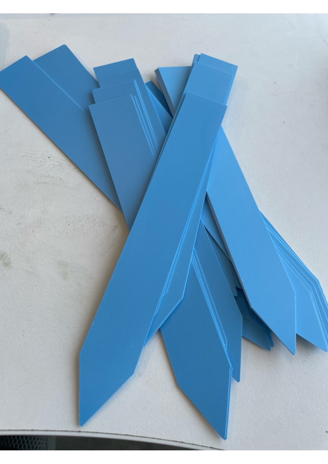 En hög med växtetikettblå plastrektanglar med vinklade ändar på en ljus yta.