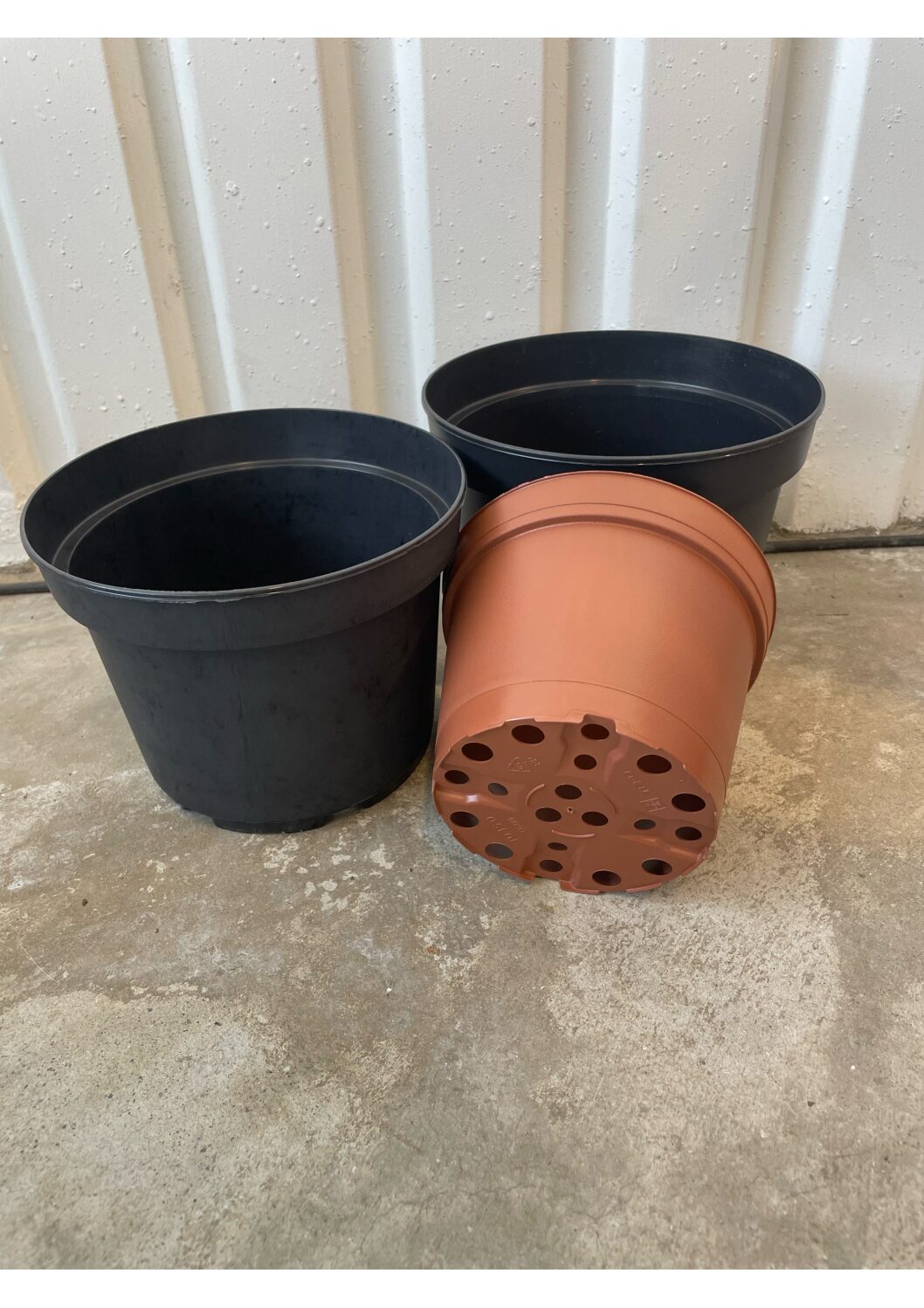 Tre Planteringskrukor plast står på ett betonggolv vid en vit vägg.