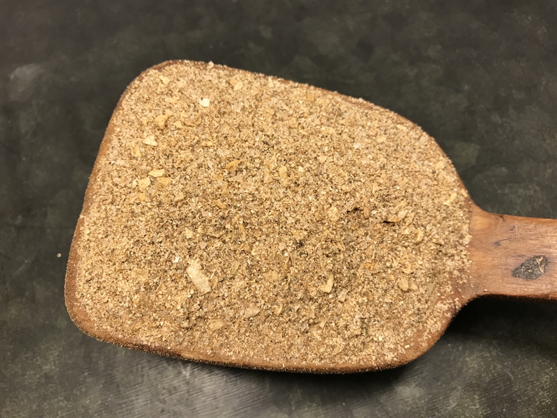 Köttbulls krydda strösslas på en träspatel på en mörk yta.