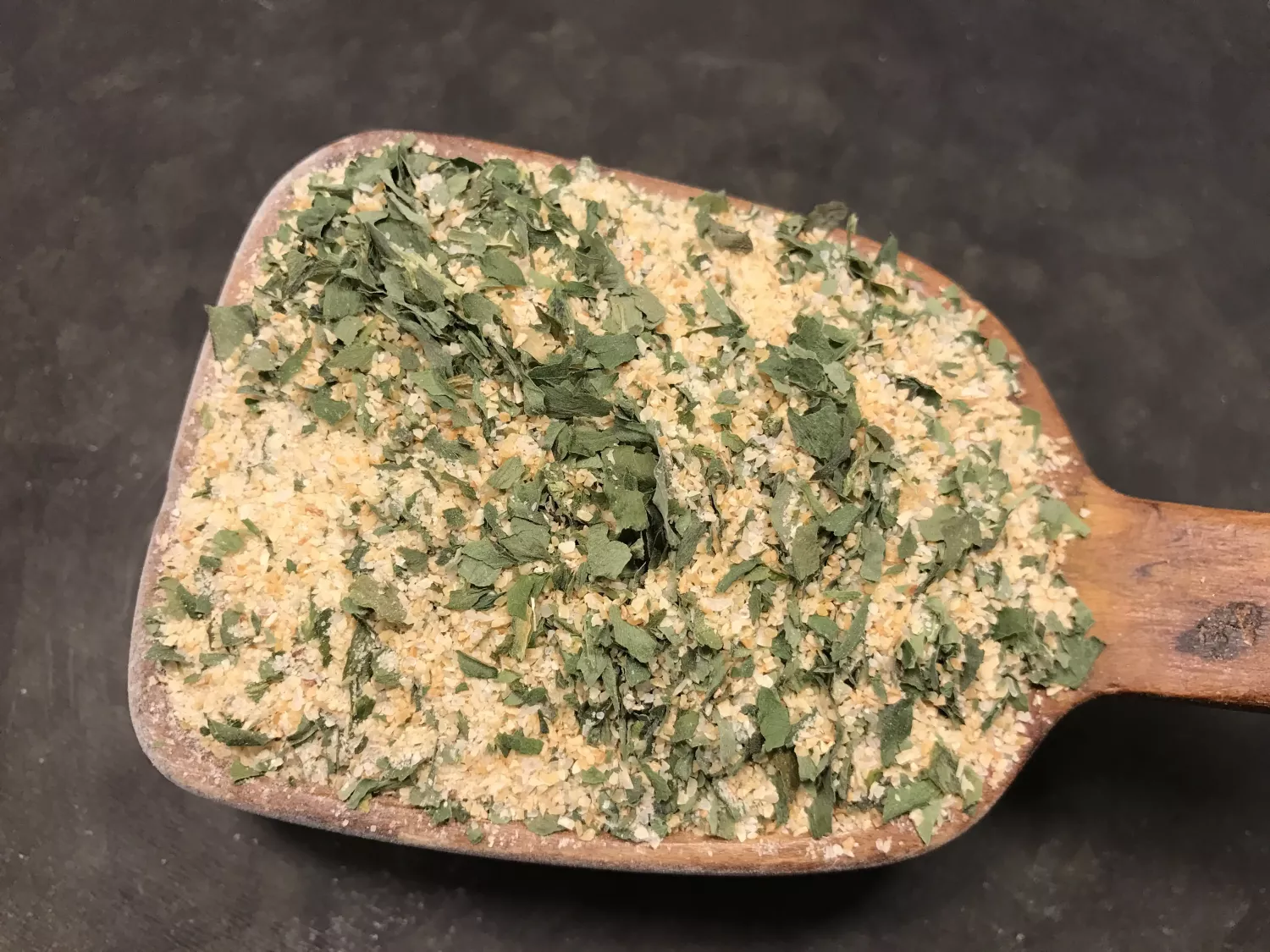 En träskopa med Kryddsmör Ramslök/vitlök innehåller örter och kryddor mot en mörk bakgrund.