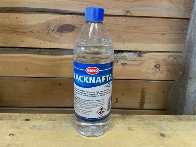 En 1L Lacknafta (lacknafta) flaska med blå kapsyl på en träyta och bakgrund.