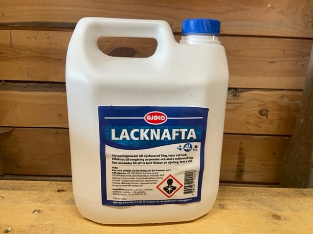 En 4L Lacknafta (lacknafta) behållare med blå etikett på en träyta.