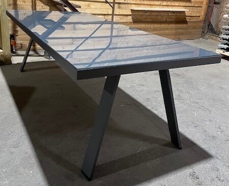 Ett modernt Metallbord med glasskiva med vinklade metallben i en industriell miljö.