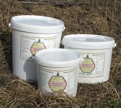 Tre stålhinkar med etiketter, placerade på torrt gräs utomhus.