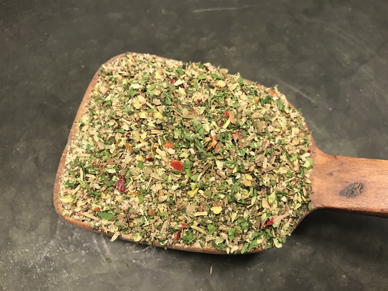 En träsked håller Örtagårdsblandning örter och kryddor mot en mörk bakgrund.