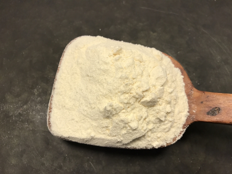 En träskopa med ostkrydda Italiensk Permensan smakpulver på en mörk yta.