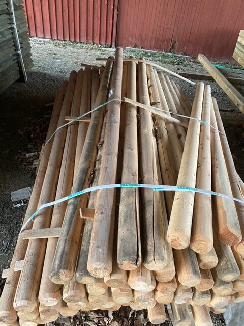 En hög med Oimpregnerade stolpar 80*2500 knyts ihop med band och placeras på marken.