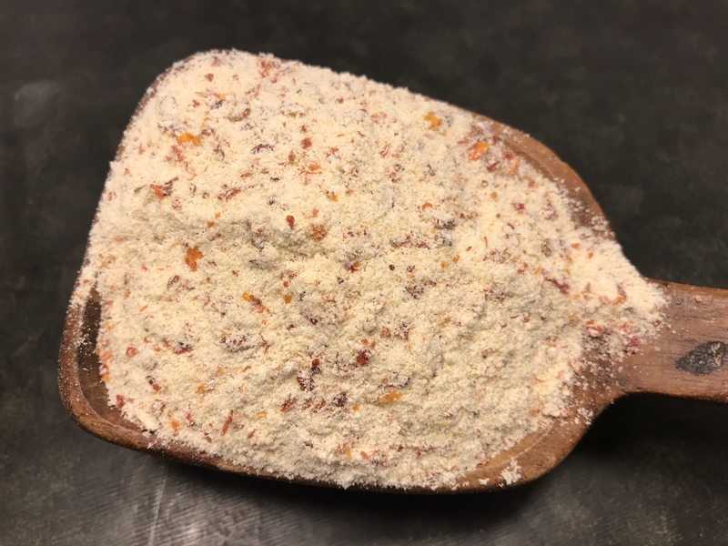 En träskopa håller grov Pastakrydda Tomat & Ost på en mörk yta.