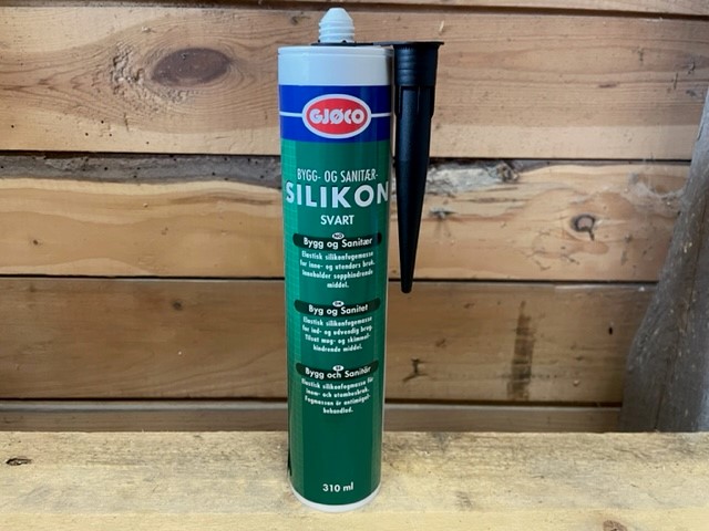 Bygg och sanitärsilikon SVART 310ml rör på en träyta mot en trävägg.