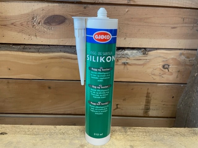 Ett Bygg och sanitärssilikon VIT 310ml rör står på trä med en trävägg i bakgrunden.
