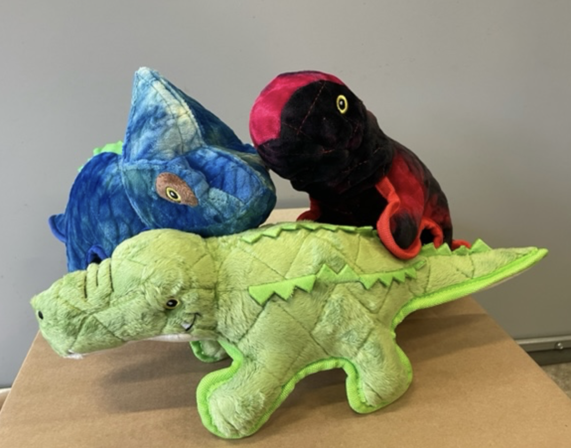 Tre DINOS med hundleksaker är grupperade tillsammans på en brun yta.