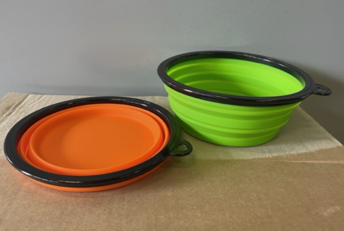 En grön expanderad och en orange kollapsad Hopfällbar skål på en brun yta.