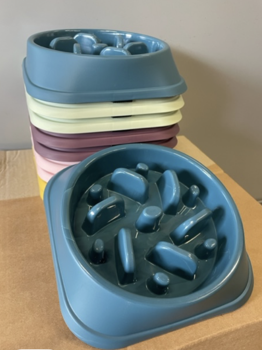 Stapel med färgglada Anti stress skålar för husdjur, med en blå skål framför, på en kartongyta.