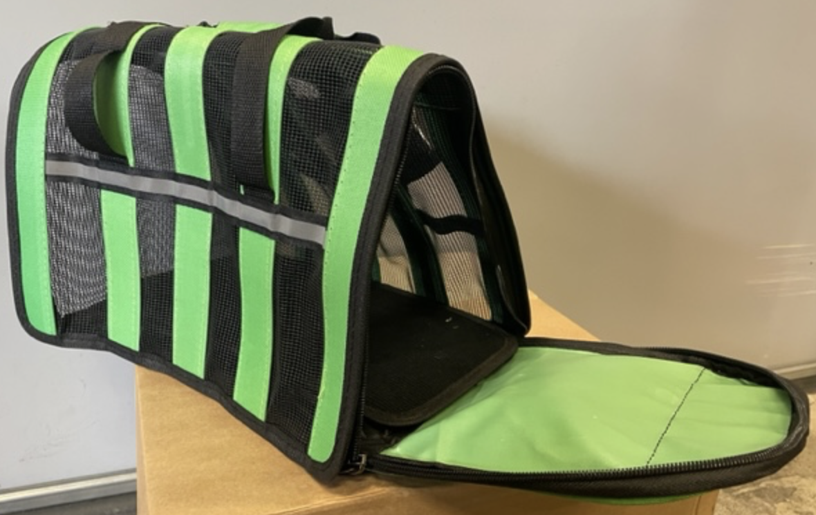 En grön och svart Transportväska - Liten transportväska för husdjur med öppen flik med dragkedja på en låda.