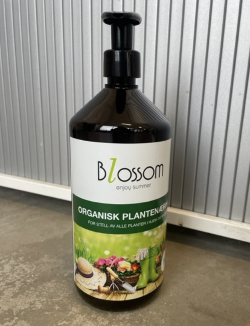 Blossom organisk planteringsnäring 1L på ett betonggolv intill en metallvägg.