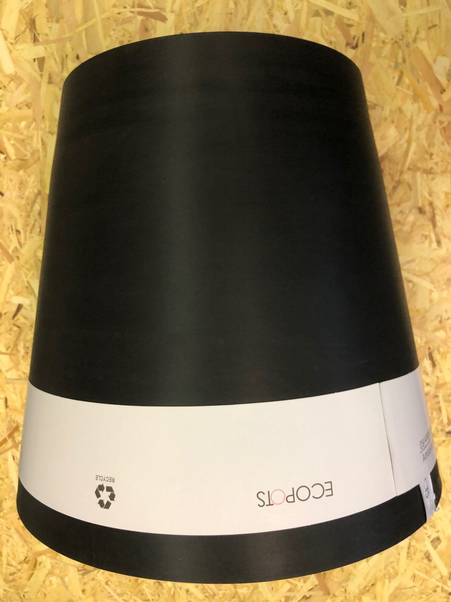 Svart växtkruka upp och ner på en träyta, med en vit etikett där det står ECOPOTS.