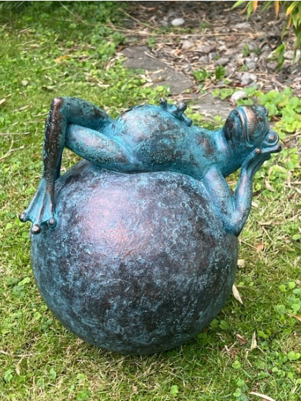 Grodstaty i brons som ligger och slappnar av ovanpå en stor texturerad sfär i gräset.