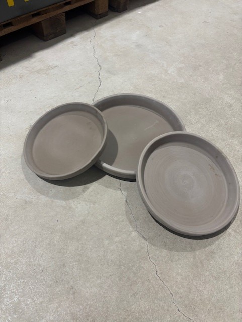 Tre FAT BASALT runda grå lertallrikar vilar på ett sprucket betonggolv.