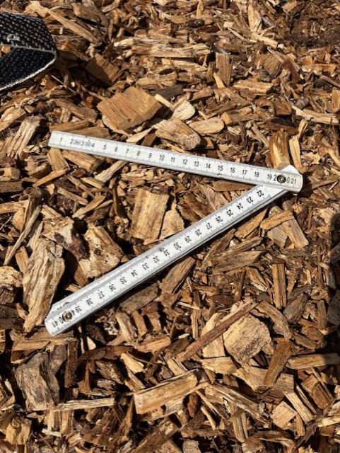 En tumstock ligger uppfälld på en bädd av träflis i starkt solljus.