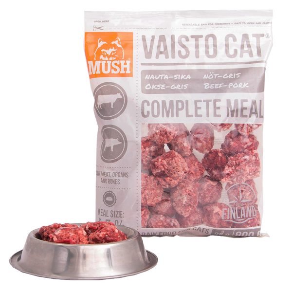 Bag of Mush Vaisto Cat Vit bakom en metallskål fylld med råa kattmatbitar.