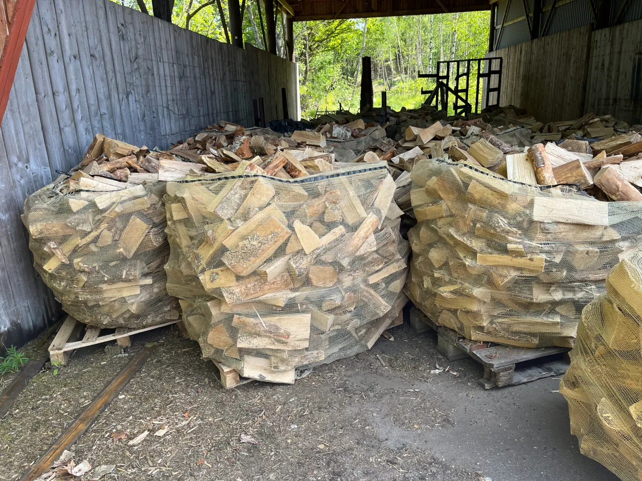 Tre Björkved 1 kubik vednät är staplade på pallar i ett täckt utomhusområde.