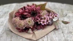 Bukett Bordeaux tork/siden visas på en träyta, inslagen i brunt papper.