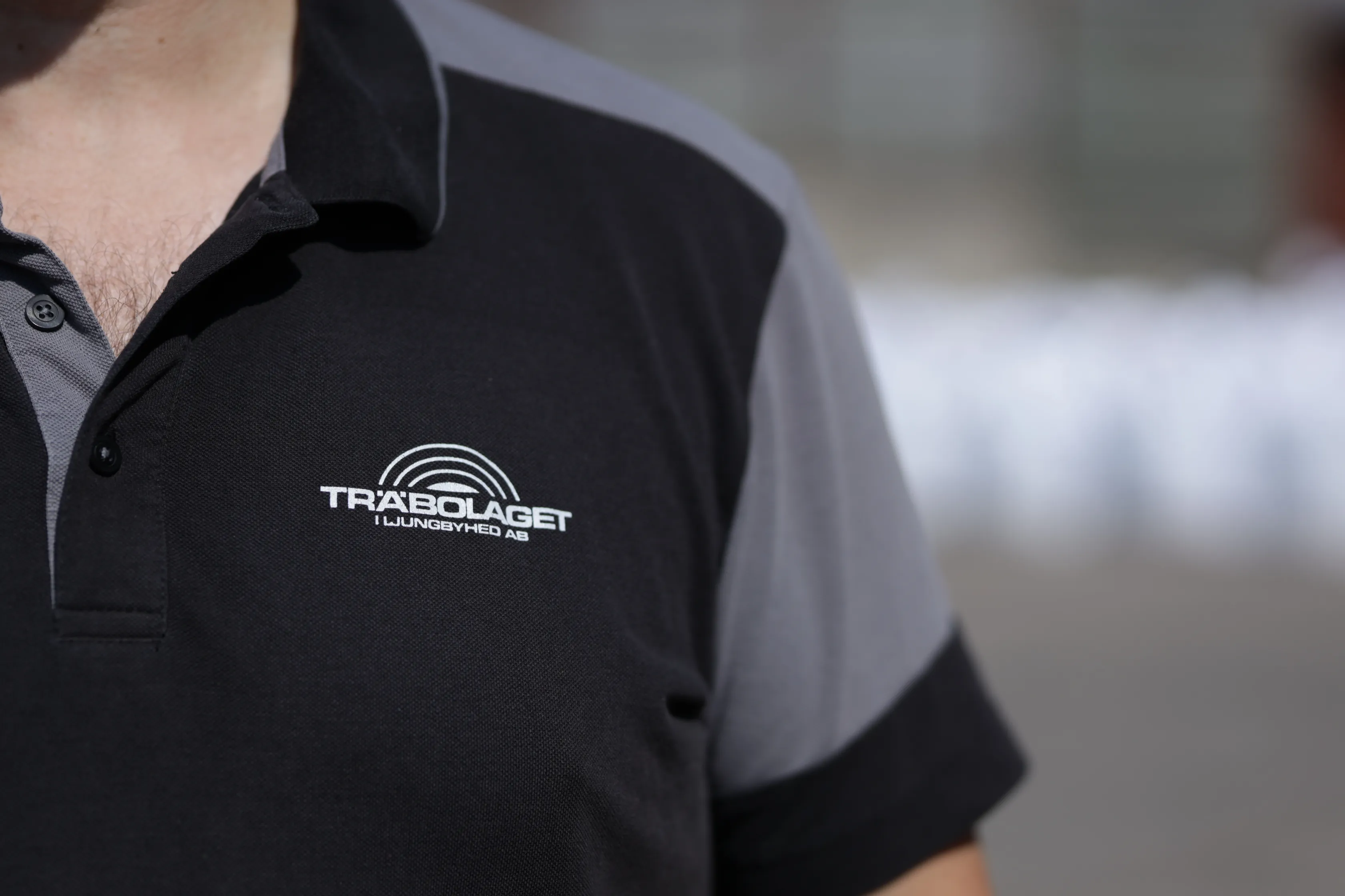 Person klädd i svartgrå TRÄBOLAGET I LJUNGBYHED AB polotröja utomhus.