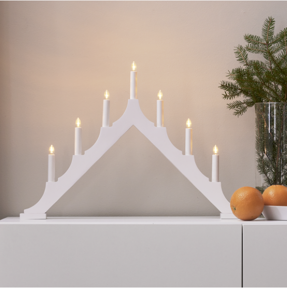 Star Trading Ljusstake Alma med tända ljus på ett skåp bredvid apelsiner och en vas med grönska.