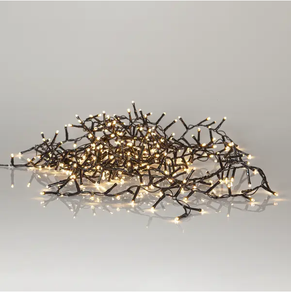 Star Trading Ljusslinga Shiny Warm White ljusslingor lyser varmt på en reflekterande yta.