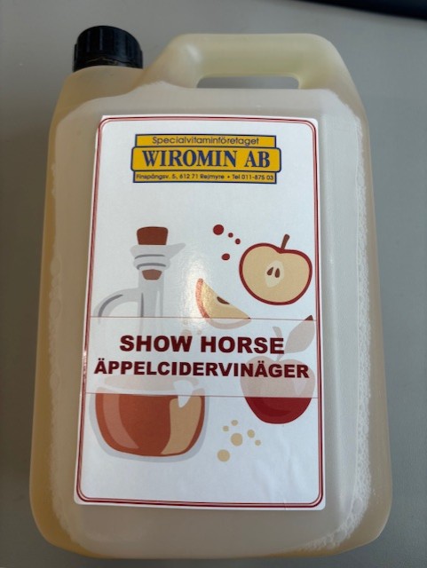 En 2,5 liters plastkanna märkt Show horse äppelcidervinäger med bilder på äpplen och vinäger.